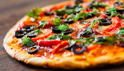 Pizza with Mozzarella cheese, salami, pepper, pepperoni, Tomatoes, olives, Spices and Fresh Basil. Italian pizza on wooden background