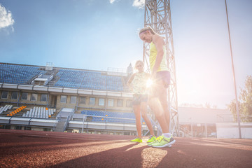 Two female sprinter athlete wearing t-shirt and shorts standing on a red running track in the athletics stadium.