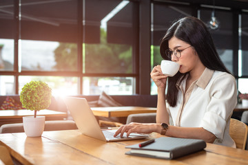 Obraz premium Asian working woman using laptop and drinking coffee in cafe. People and lifestyles concept. Technology and business theme. Freelance and occupation theme. Workaholic in overnight concept.