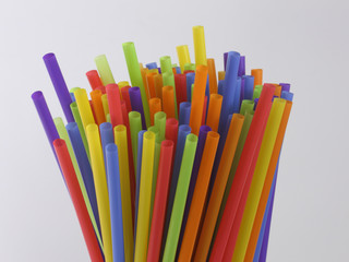 A bundle of colorful, single-use plastic straws are shown on display, stick up and isolated against...