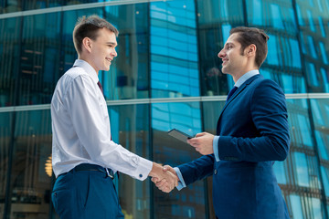 Two businessmen shaking hands after successful deal in front of modern building