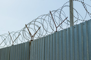 Metal fence with barbed wire on blue sky background