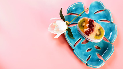 cheesecake with fruit dessert on a decorative plate, flowers on a pink background, copy space, Flat lay
