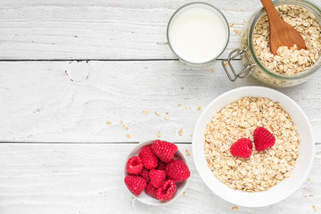 Ingredients for healthy breakfast - miilk, raspberries and oat muesli on white wooden table. top view