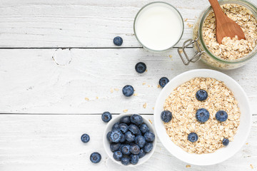 Ingredients for healthy breakfast - miilk, blueberries and oat muesli on white wooden table. top view