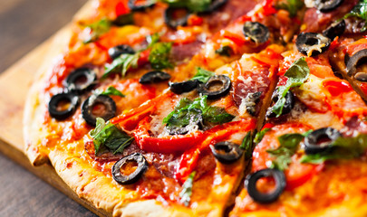 slices of Pizza with Mozzarella cheese, salami, pepper, pepperoni, Tomatoes, olives, Spices and Fresh Basil. Italian pizza on wooden background