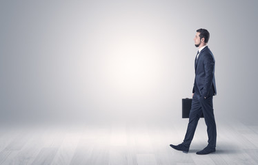 Successful businessman walking in front of an empty wall with briefcase on his hand
