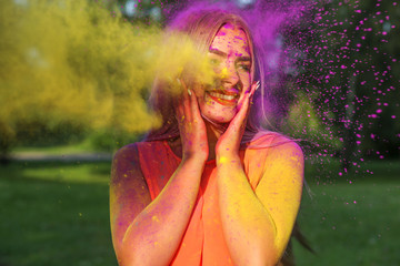 Cool young woman posing with exploding yellow paint at summer Holi festival