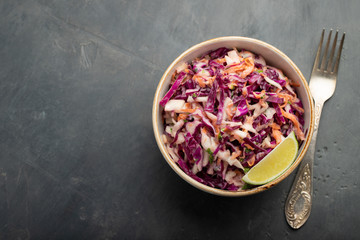 Purple cabbage and carrot salad with mayonnaise in a white bowl on a black background. Classic coleslaw. Diet vegetarian dish. Top view with copy space