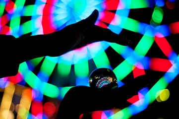 Ferris wheel through a glass ball on the palm of your hand. The atmosphere of celebration and rest. Evening adventure. Bright color. Hand silhouette