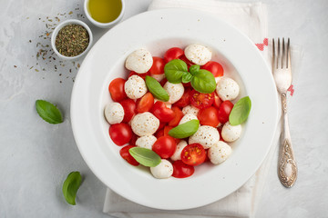 White plate of classic delicious caprese salad with ripe tomatoes, mozzarella and fresh basil leaves on gray concrete background. Italian food. The concept of a healthy vegetarian diet. Top view