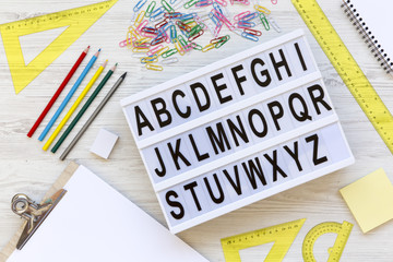 Back to school concept. Letters from A to Z. English alphabet on modern board and accessories for study over white wooden table, top view. From above, flat lay, overhead.