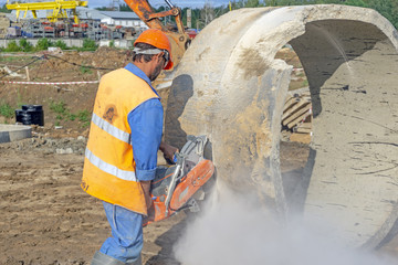 Worker at the construction site cuts the ring for the well with concrete cutters