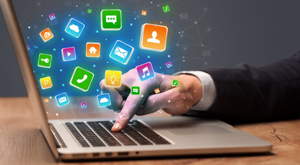 Businessman hand typing on laptop with flying application icons around
