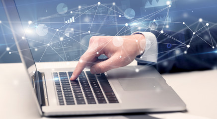 Businessman typing on laptop with linked reports charts grapghs around
