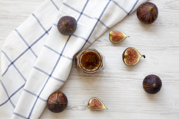 Glass jar of fig jam and fresh figs on white wooden background. Top view, from above.