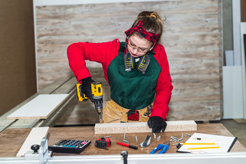 Beautiful woman carpenter drilling wooden plank, carpentry