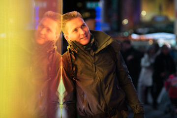 Stylish young man with his reflection on background with blurred lights of the city at night