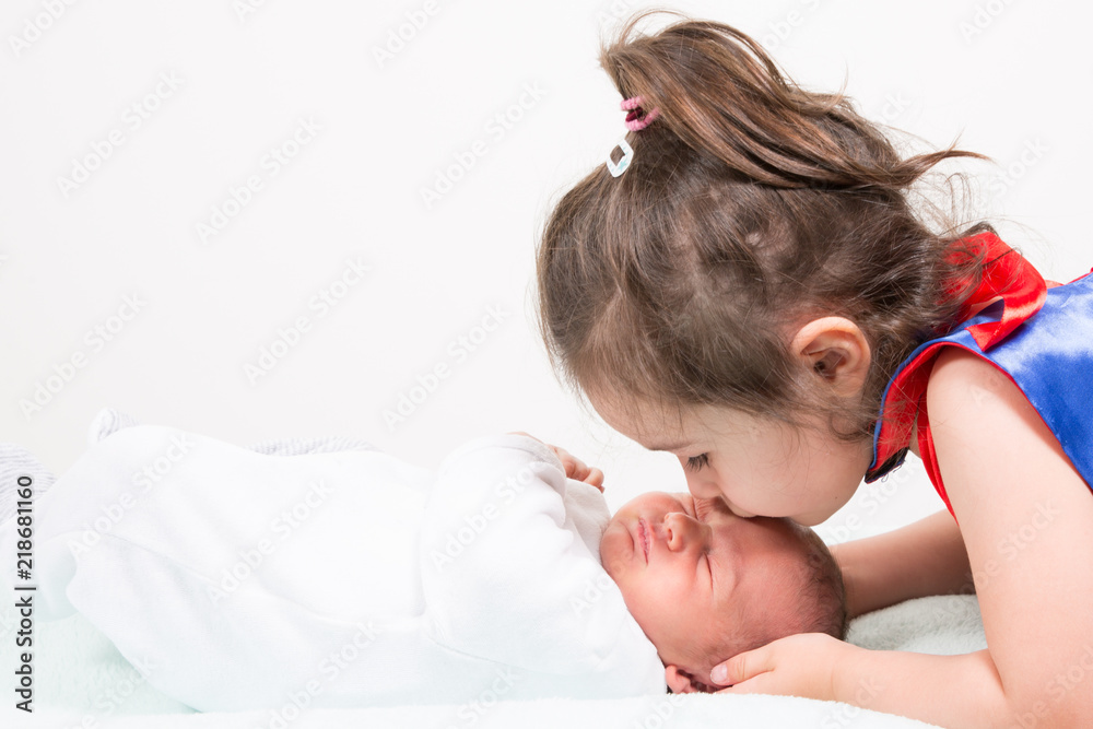 Wall mural young little sister hugging her newborn brother baby on a light background