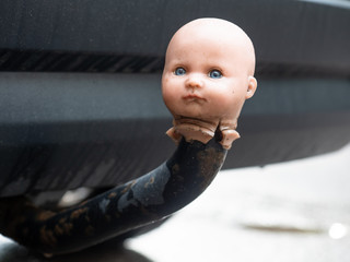 Doll's head impaled in irreverent manner to car tow-bar, with bumper of car in background 