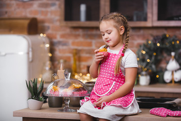 Little cute girl in the kitchen eating cupcakes