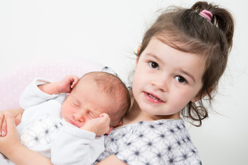 older girl sister hugs baby boy newborn in white pajamas sleeping