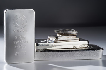 Minted silver bars and coins against a gray background. Selective focus.