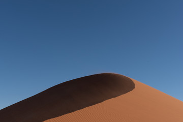 Fototapeta na wymiar Shadow curve of a red sand dune with blue sky, Namibia