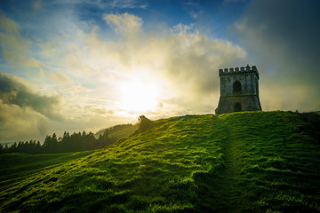 a fortress on a green hill during a beautiful sunset