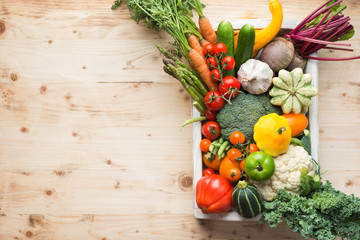 Fresh organic vegetables in a white tray on wooden pine table, top view, copy space, selective focus