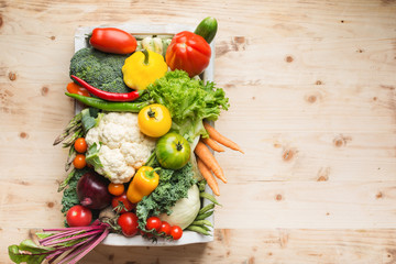 Fresh organic colorful vegetables in a white tray on wooden pine table, top view, copy space, selective focus