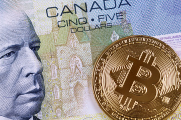 A close up image of a Canadian five dollar bill with a golden bitcoin