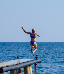 A beautiful girl in a blue bikini jumps from the pier into the water. Jumping in the sea.