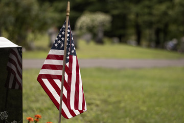 Cemetery graveyard with headstones, amaerican flag, grass and road during a cloudy day.