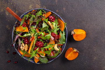 Salad with persimmon, arugula, pomegranate seeds, nuts, dried cranberry on dark background. Flat lay, copy space