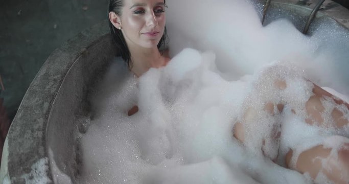 Attractive girl in the bath blowing foam and smiling