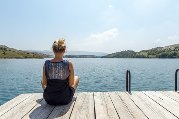 Fototapeta na wymiar Back view young woman sitting by the lake and relaxing 