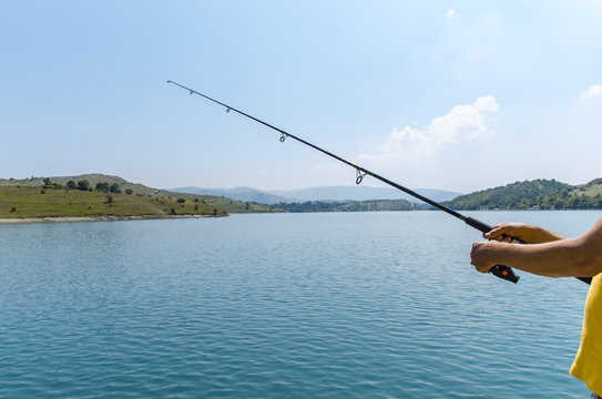 Unrecognizable man holding fishing rod next to beautiful lake on beautiful sunny day 