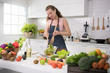 Healthy young woman in a kitchen preparing vegetables for healthy meal and salad