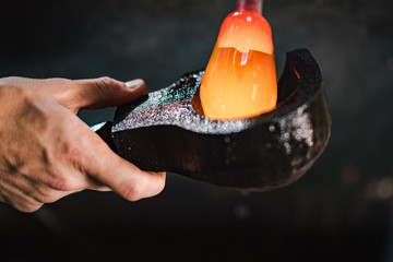 A glassmaker shapes an orb of molten glass in a wooden mold