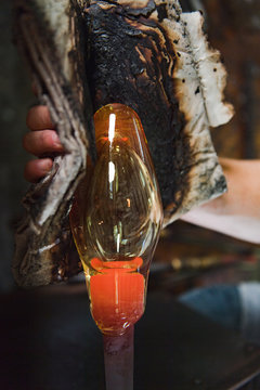 A glassmaker cools and shapes an orb of hot glass
