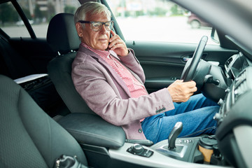 Side view portrait of successful senior businessman sitting in luxury car and speaking by smartphone, copy space