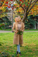 Beautiful elegant woman standing under the rowan tree in autumn park