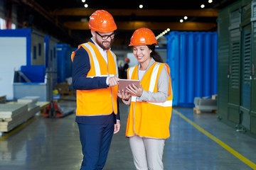 Portrait of female factory worker talking to businessman wearing hardhat while using digital tablet...