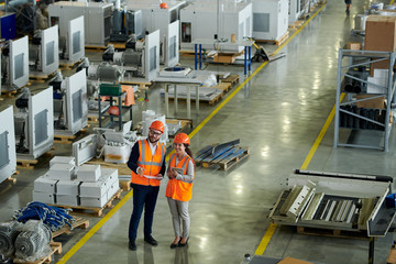 High angle full length portrait of cheerful young woman wearing hardhat giving tour of production...