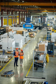 High angle full length portrait of bearded businessman wearing hardhat inspecting production workshop accompanied by smiling young woman, copy space
