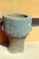 An old-style stone mortar in front of a house made of clay.