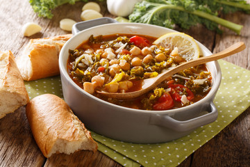 Soup of chickpeas, kale, tomatoes, garlic and potatoes with lemon close up in a bowl on the table. horizontal