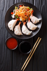 Traditional Asian dumplings stuffed with shrimps with fresh vegetable salad close-up on a plate and soy and tomato sauces. Vertical top view
