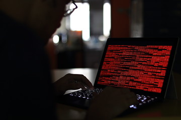 Computer Hacker silhouette typing on computer in a dark room. Working on binary code technology....